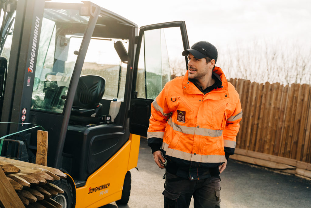 Portrait d'un cariste en tenue orange près de son chariot élévateur