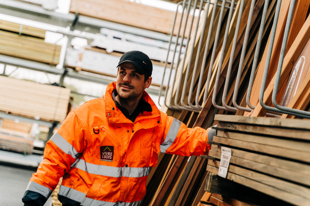 Ouvrier en tenue orange au travail dans un stock de bois